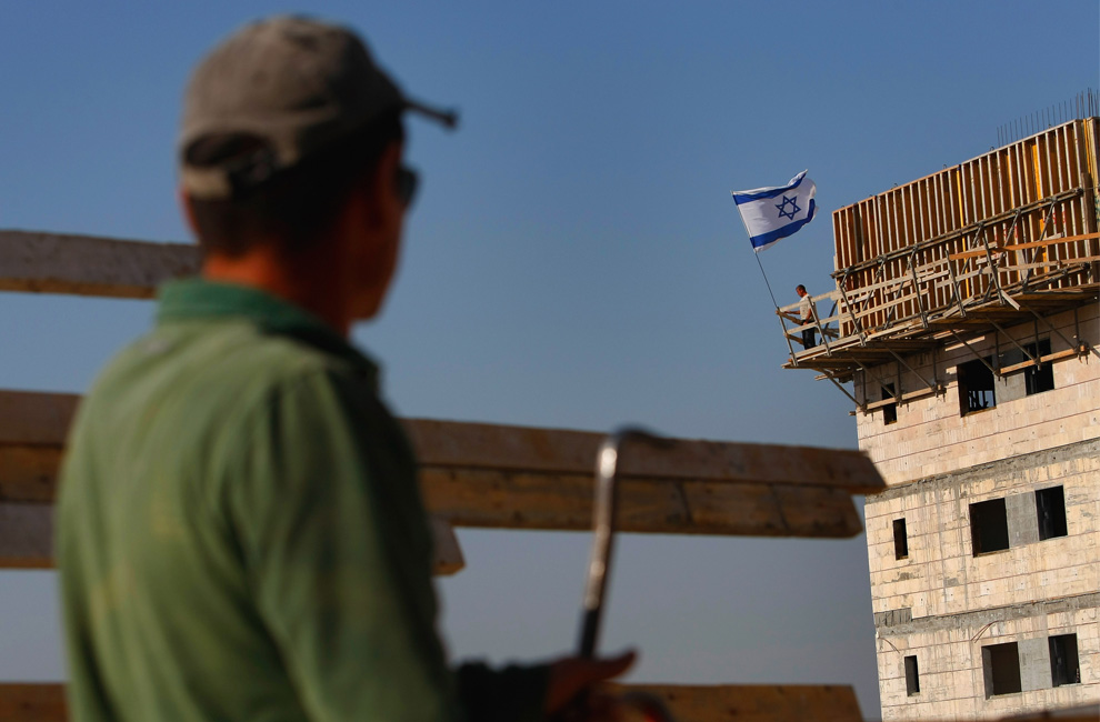 Berdiri di samping bendera Israel dalam mengembangkan malam angin pembangun beristirahat setelah seharian bekerja keras di pembangunan perumahan baru di pemukiman Yahudi Alpha Menashe 8 Juni 2009 di Tepi Barat.  (David Silverman / Getty Images)