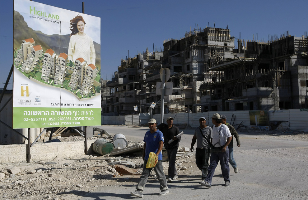 Pekerja Palestina berjalan melewati papan reklame perumahan draft baru di pemukiman Yahudi Maale Adumim di Tepi Barat yang diduduki, 7 Juni 2009.  (Menahem Kahana / AFP / Getty Images)