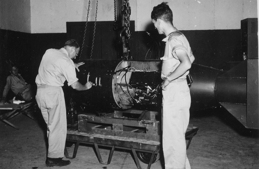 5. Командир А.Ф. Бирч (слева) нумерует бомбу под кодовым названием «Малыш» перед погрузкой ее на трейлер в здании Ассамблеи №1 перед конечной погрузкой бомбы на борт бомбардировщика B-29 Superfortress "Enola Gay" на базе 509-ой сводной группы на острове Тиниан у Марианских островов в 1945 году. Физик доктор Рамсей (справа) получит Нобелевскую премию в области физики в 1989 году. (U.S. National Archives)