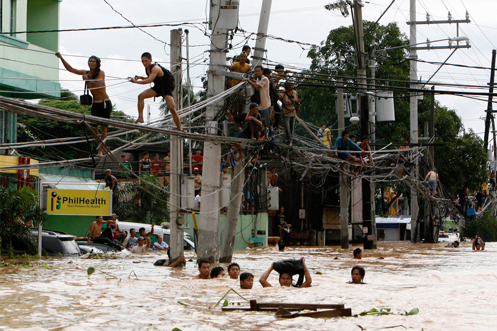 5. Жители Каинта Ризал к востоку от Манилы идут по электропроводам, в то время как другие идут вброд по шею в воде, принесенной сюда тайфуном Кетсана 27 сентября 2009 года. (REUTERS/Erik de Castro)