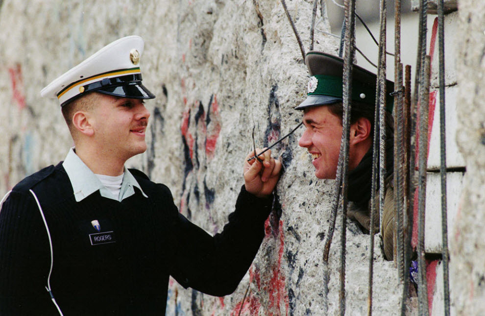 17. Служащий США Стив Роджерс из Оакланда. Калифорния, разговаривает с солдатом пограничной службы Восточной Германии Майком Стаапсом, который выглядывает из отверстия в восточной части Берлинской стены 26 марта 1990 года. (Herbert Proepper, AP)