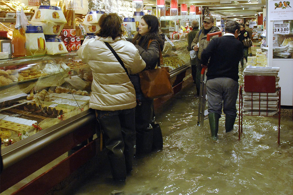 25. Покупатели стоят в полузатопленной кондитерской в Венеции 1 декабря 2008 года. Туристам и жителям города пришлось ходить по затопленным улицам на деревянных настилах. Метеослужба «Centro Maree» сообщила, что уровень Адриатического моря поднялся на 1,56 метров. (REUTERS/Michele Crosera)