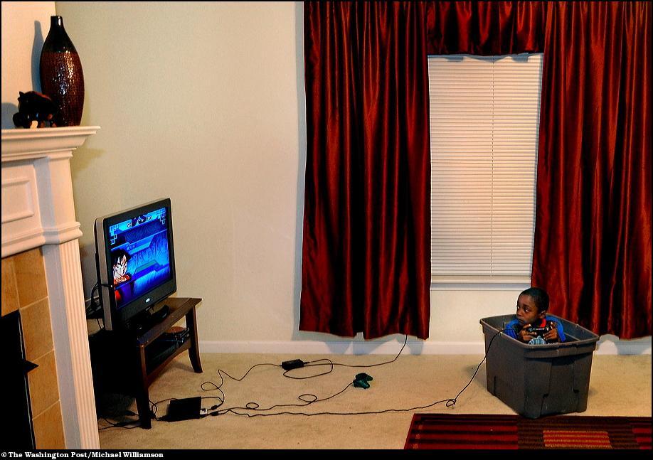 8) Милик Вайт играет в видеоигру сидя в пластиковой коробке для игрушек.