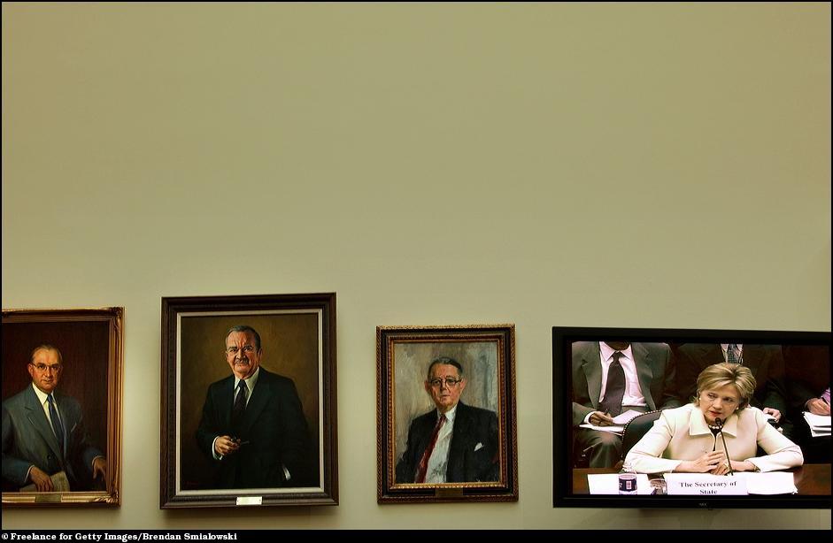 17) Госсекретарь Клинтон вещает из плазмы в окружении портретов.