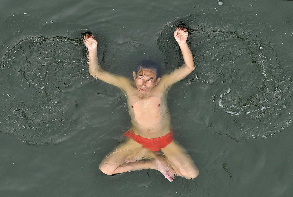 Мужчина во время летней жары сидит в воде в Тяньцзине, Китай