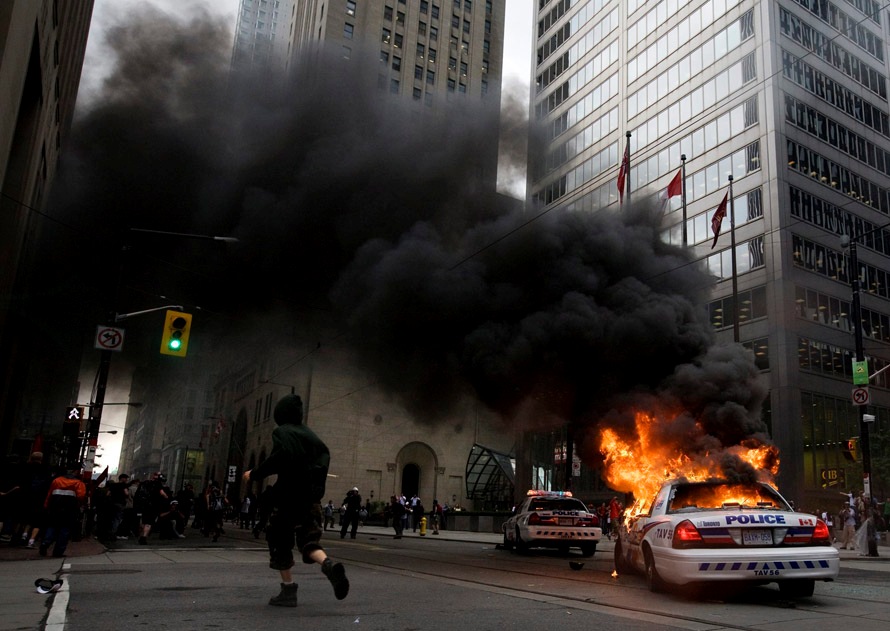 Активист проходит мимо горящего полицейского автомобиля в деловом центре Торонто в субботу, 26 июня, во время беспорядков, которые прошли при проведении саммита Большой Двадцатки