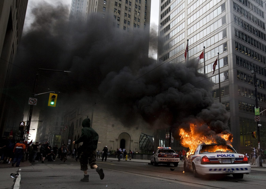 Активист пробегает мимо горящего полицейского автомобиля в финансовом центре Торонто во время акций протеста, которые прошли в Торонто во время саммита Большой Двадцатки