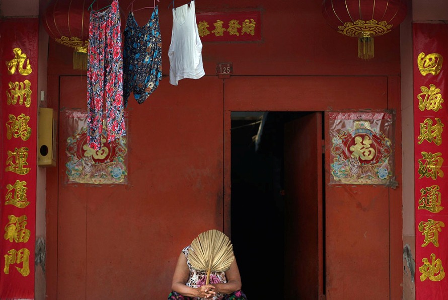 Китаянка держит веер, сидя перед своим домом в пекинском районе Хутонг