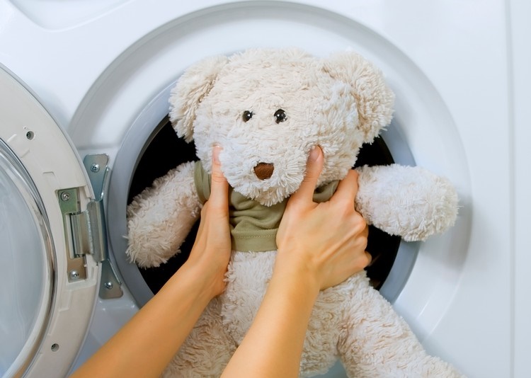 Woman loading fluffy toy in the washing machine