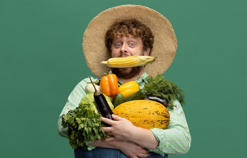 Redheaded bearded man, farmer with vegetables harvest isolated over green studio background.