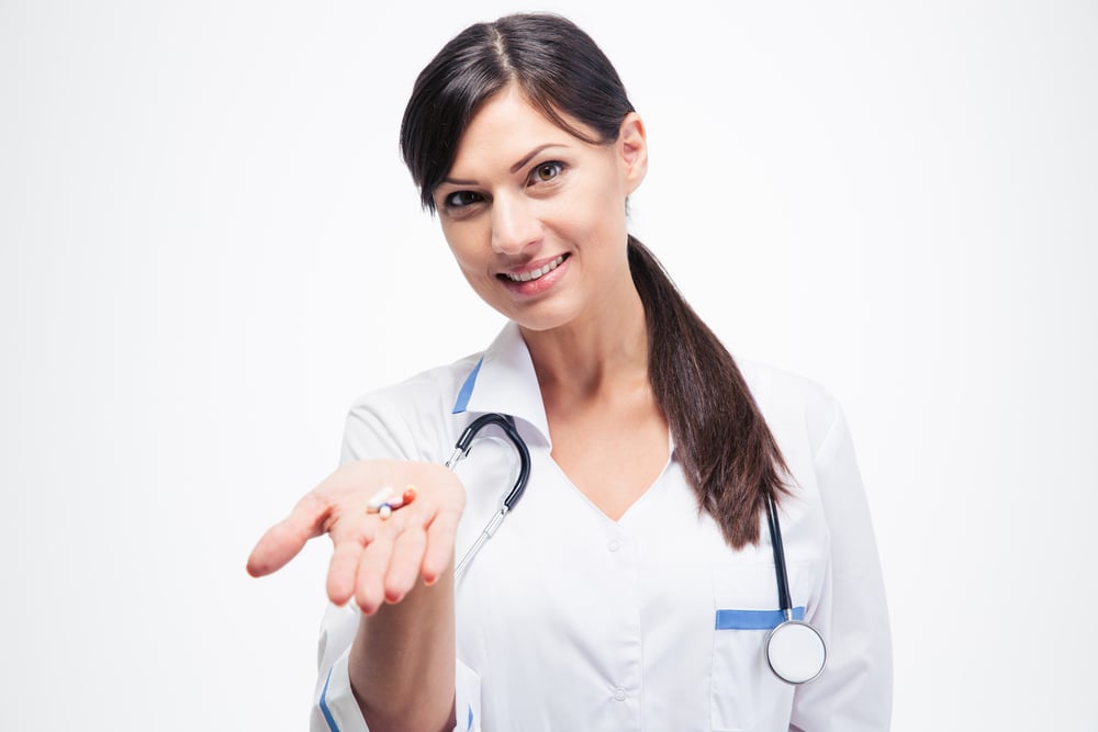 Bigpicture ru smiling female doctor holding medication isolated on a white background. looking at camera