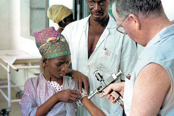 Женщина в Африке получает прививку от оспы: медицинский работник делает укол в плечо пациентке на открытом воздухе