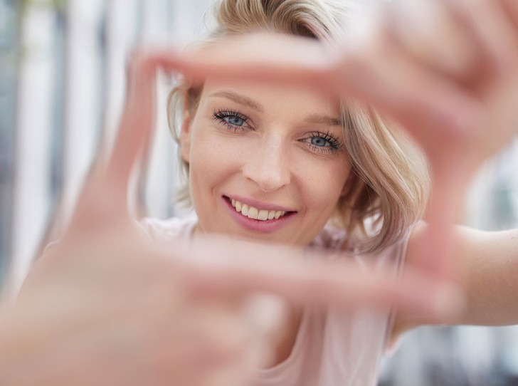 Девушка делает кадр руками в форме сердца на фоне улицы, улыбается в камеру