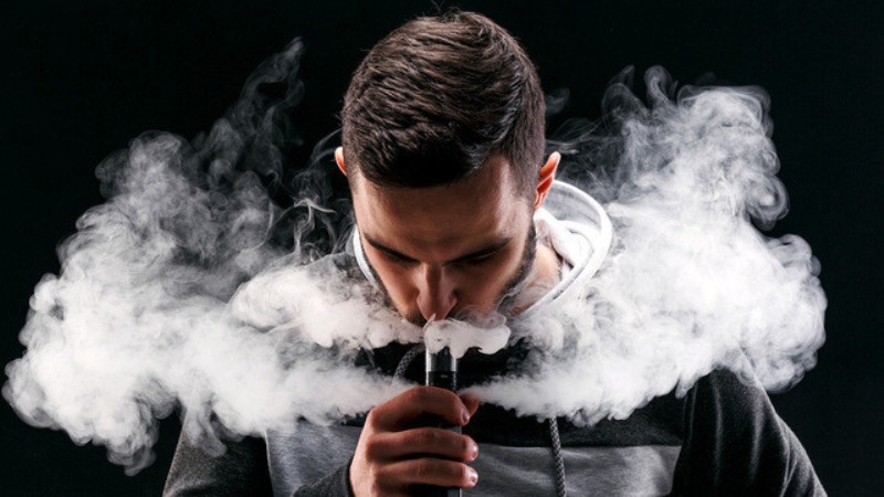 Young man vaping e cigarette with smoke on black