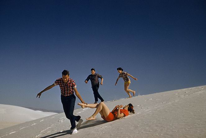 Teenagers run and play on large white sand dunes.