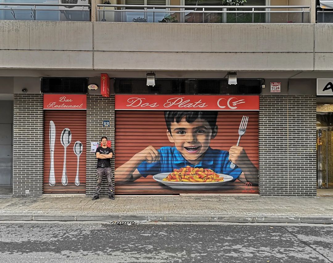 Мурал мальчика с пастой на воротах ресторана Dos Plats работы Ориола Аруми