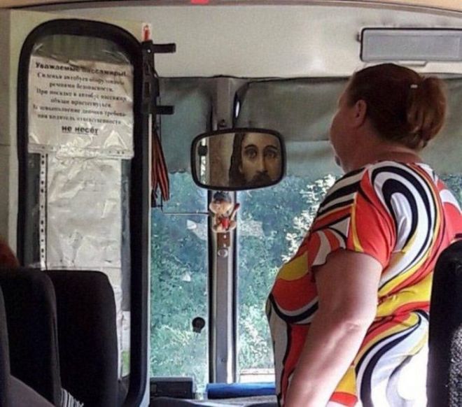 Женщина в автобусе смотрит в зеркало заднего вида, где отражается лицо похожего на Иисуса