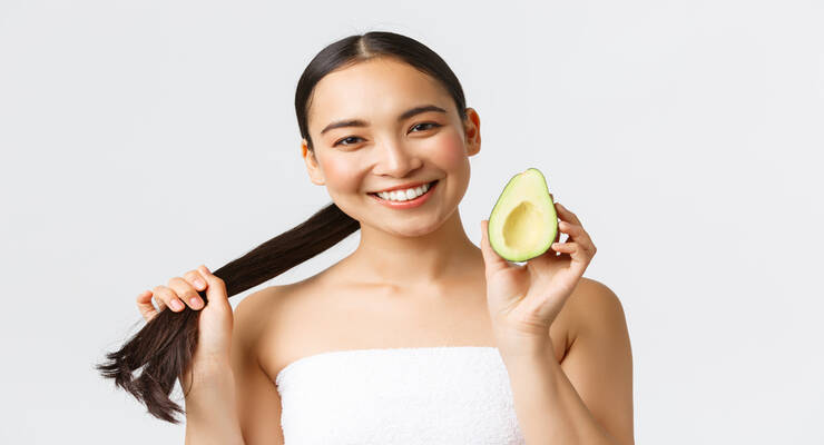 Beauty, personal care, spa and skincare concept. close up of happy good looking asian woman in bath towel, showing hair and avocado, promo of shampoo, haircare masks or conditioner