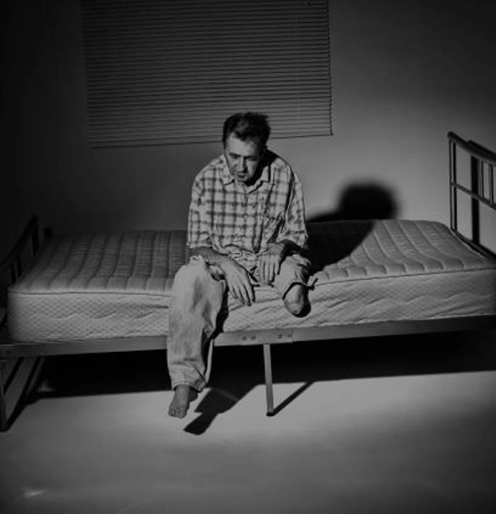 Одинокий инвалид на голом матрасе в пустой комнате, символ социальной изоляции