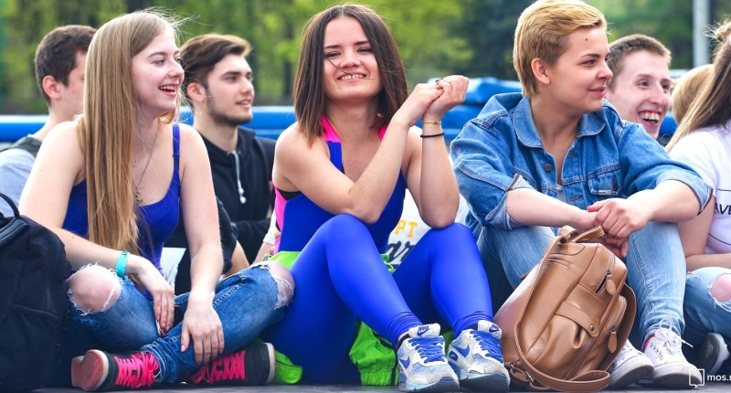 Группа улыбающихся зумеров подростков сидят на улице в яркой одежде и обсуждают что-то весело