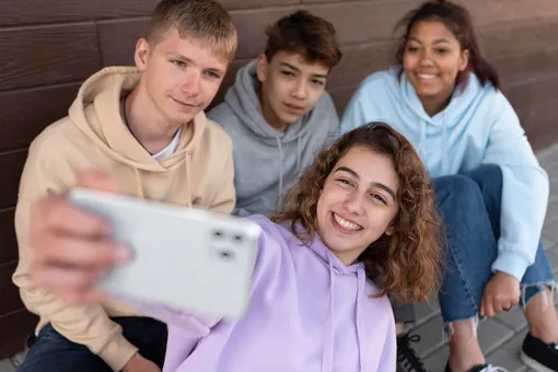 Компания подростков-зумеров делает селфи на смартфон на фоне городской стены