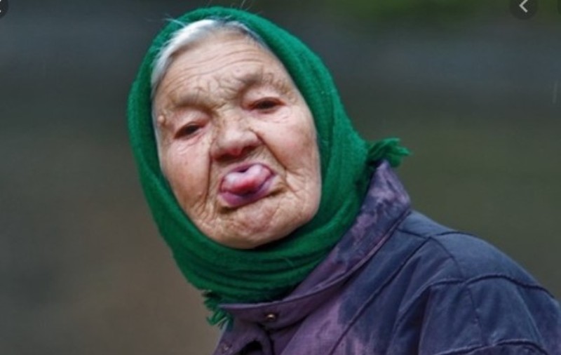 Весёлая пожилая женщина в платке показывает язык в камеру