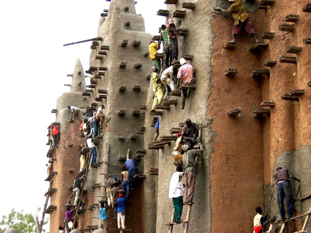 Группа мужчин на лесах у стены Великой мечети Дженне во время нанесения глиняной штукатурки