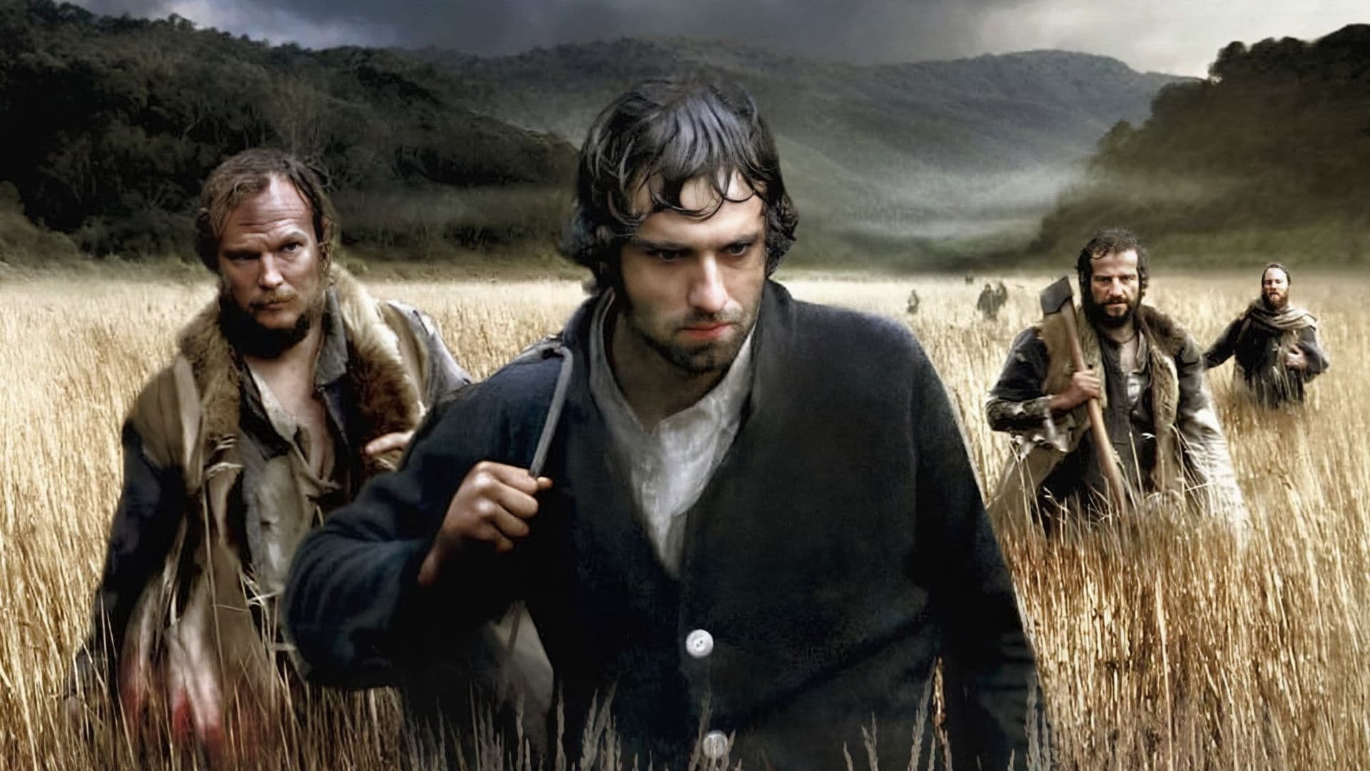 Двое обессиленных беглецов в рваной одежде бредут по скалистому берегу среди густых зарослей