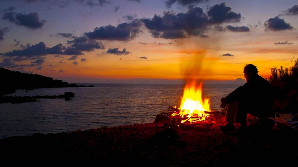 Ночной костер, отражающийся в темной воде реки, вокруг &mdash; стена черного леса
