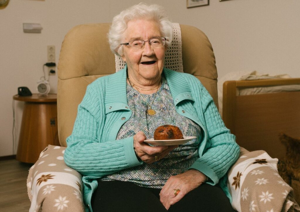 Пожилая женщина с седыми волосами улыбается за чаепитием