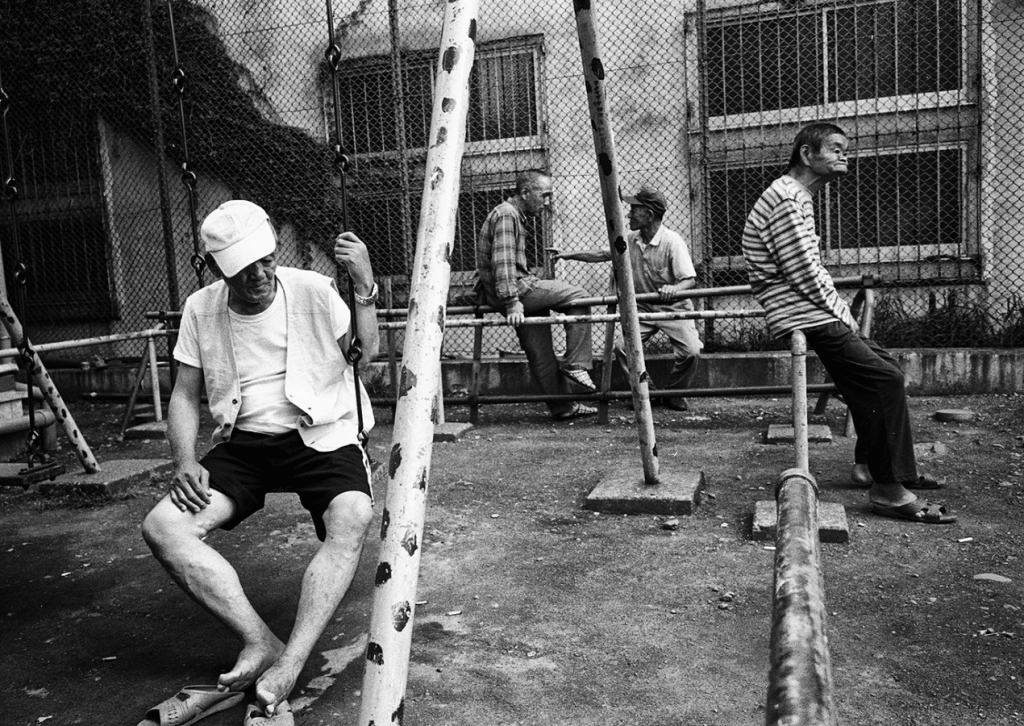 Группа пожилых и бездомных мужчин на улице на фоне зарешеченных окон