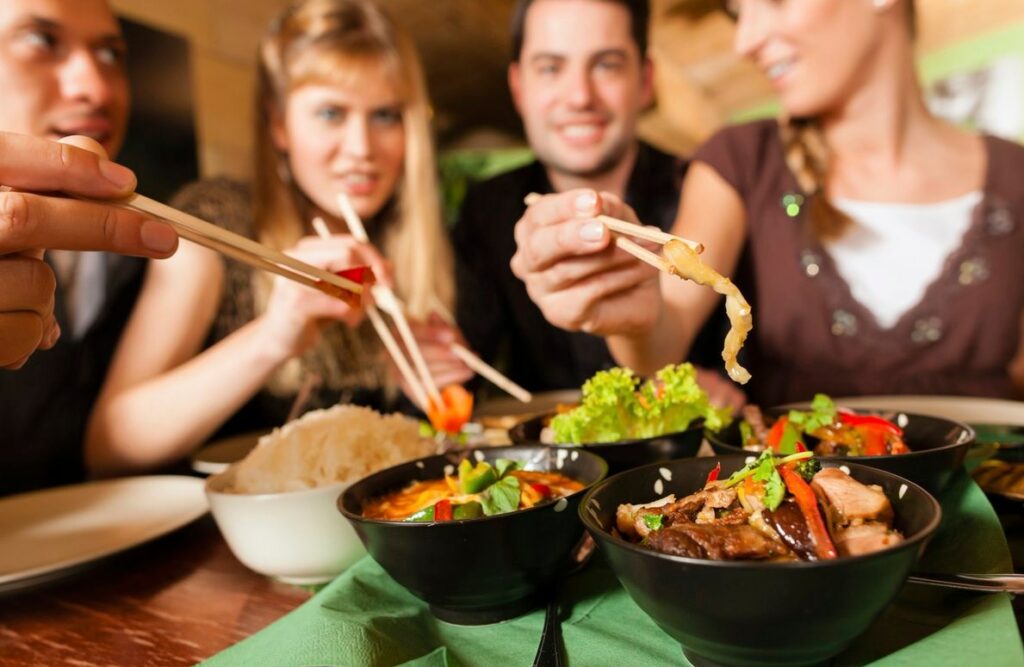 Группа людей в азиатском ресторане ест традиционные блюда палочками