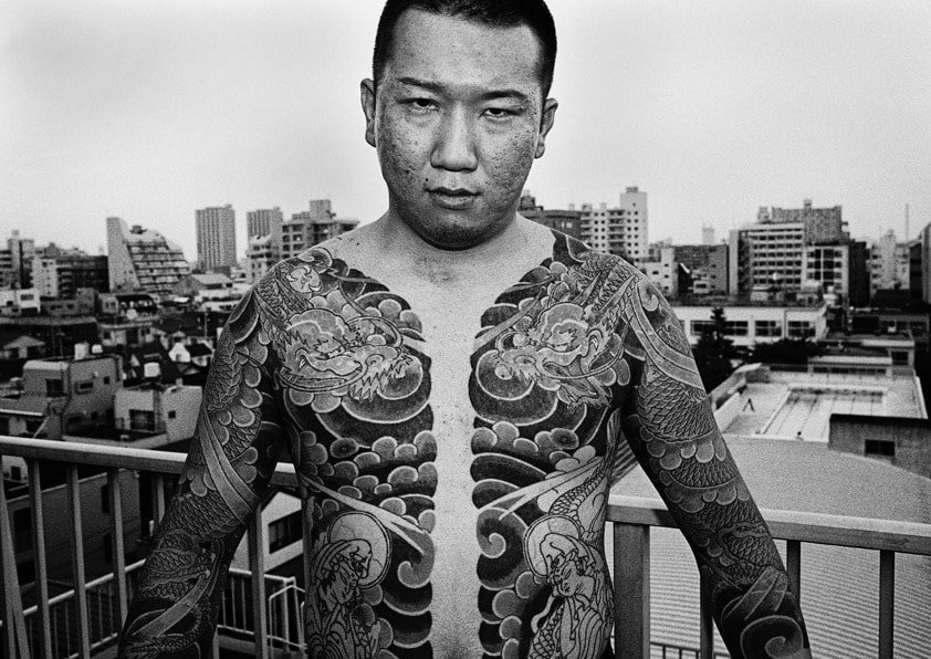 Член якудза с татуировками на груди и руках позирует без рубашки, серьезный взгляд