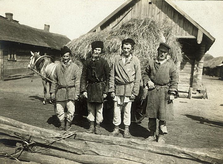 Пожилой крестьянин в традиционной русской рубахе сидит задумчиво на лавке у избы