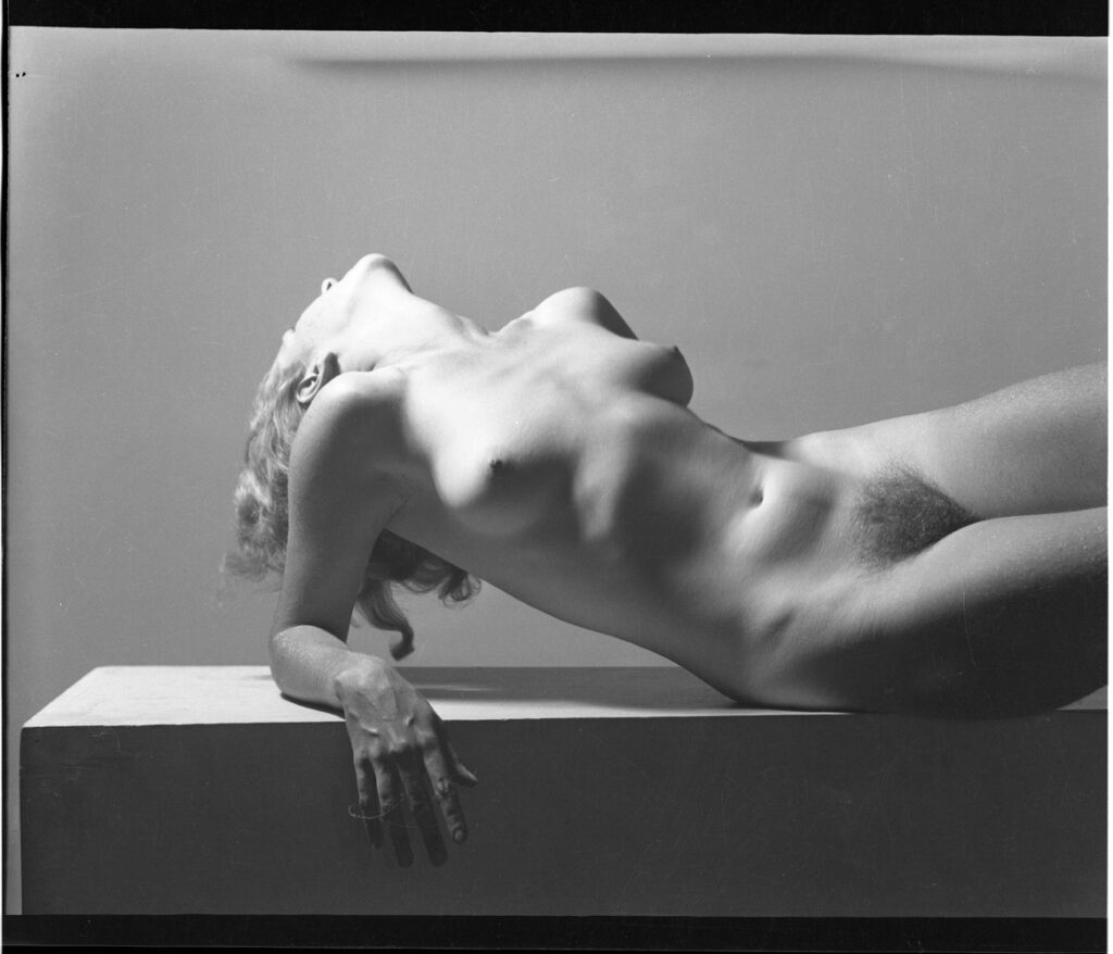 Обнаженная женщина лежит на постаменте в изогнутой позе с рукой у лица &mdash; эротический торс в стиле Уильяма Мортенсена