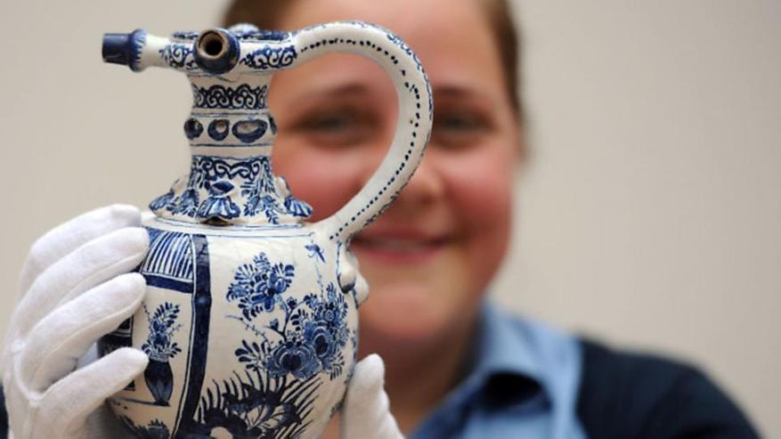 Девушка в перчатках держит бело-голубой сосуд