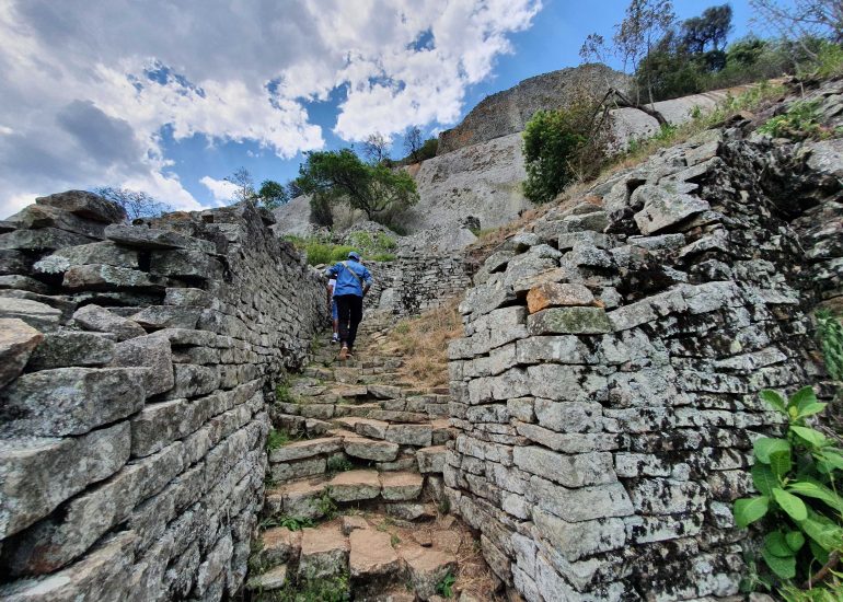 Человек поднимается по лестнице на руинах Большого Зимбабве