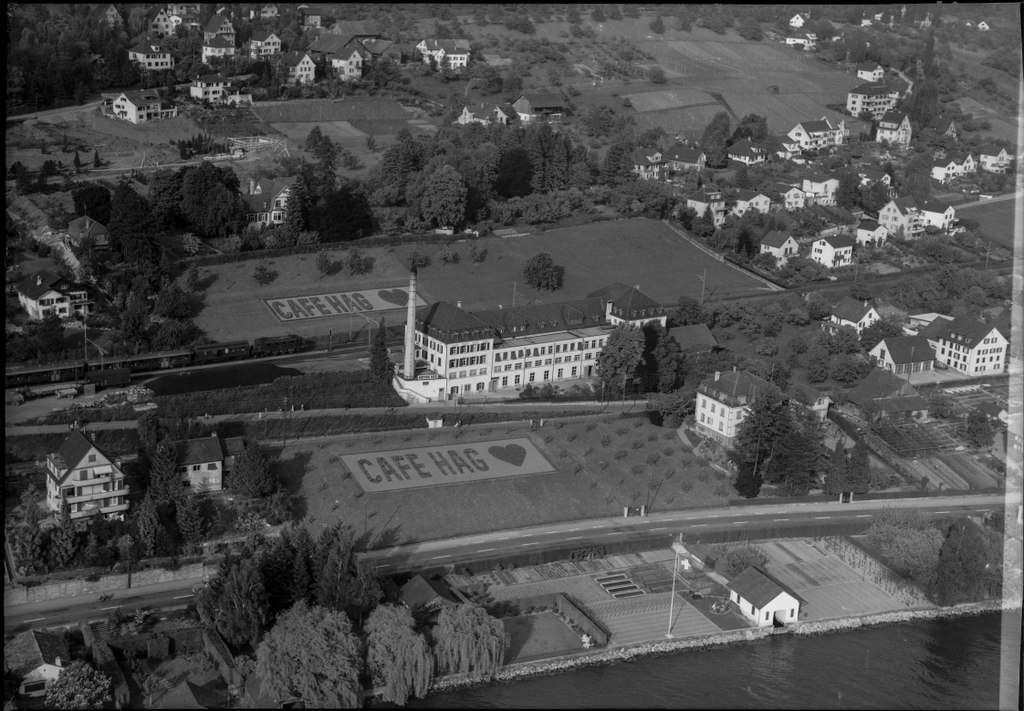 Старинное черно-белое фото: длинное здание кофейной фабрики Kaffee HAG в Бремене с рядами окон и дымящейся трубой.