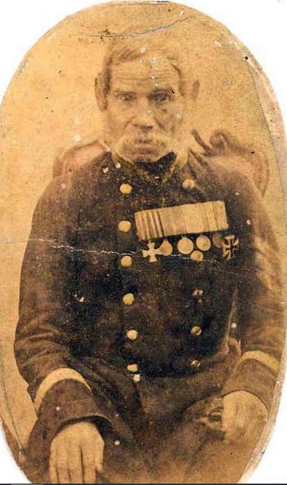 Пожилой бывший солдат в старой военной форме с медалями сидит на лавке у избы