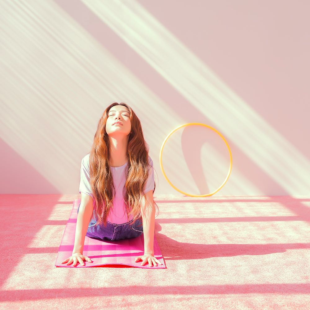 Девушка в розовом топе занимается йогой на коврике с обручем