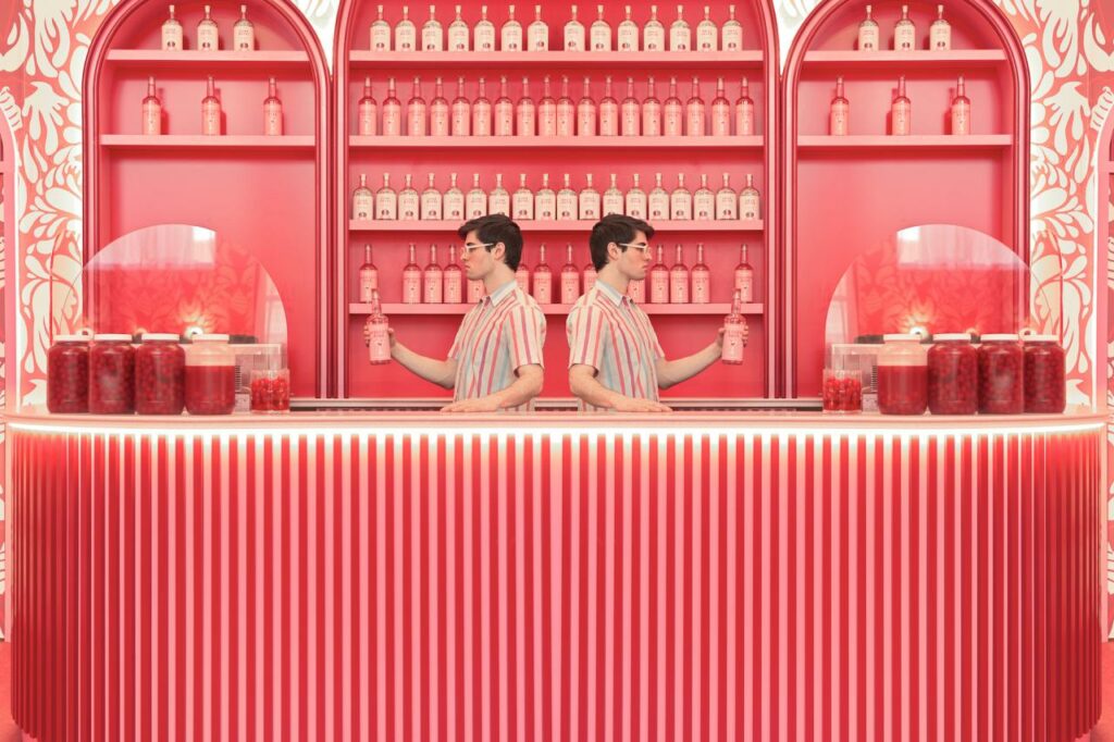 Два мужчины в полосатых рубашках наливают напитки за барной стойкой в красном интерьере 