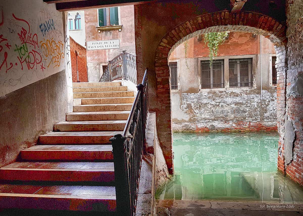 Фасад венецианского дома с облупившейся штукатуркой и следами высолов от солёной воды, у самой кромки канала