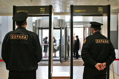 Двое охранников в форме стоят у проходной промышленного предприятия