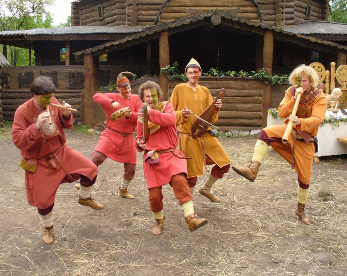 Скоморохи в ярком костюме с бубенцами танцует на улице 