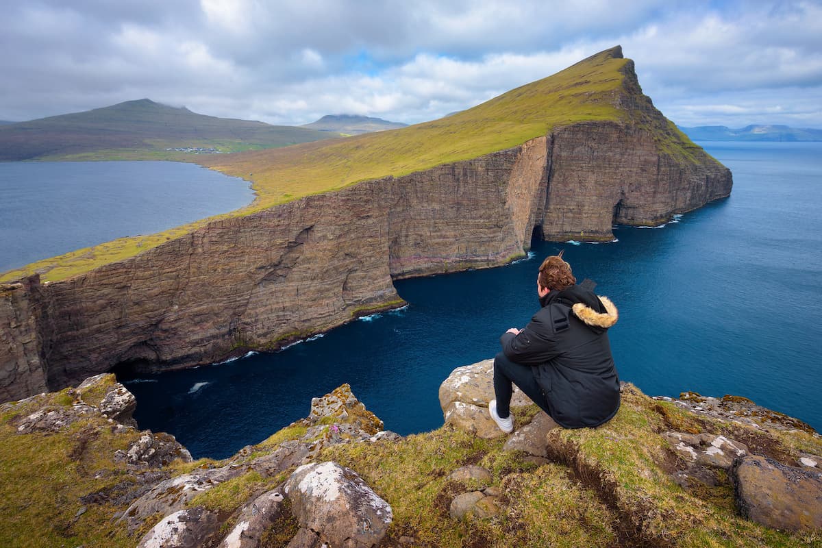 Турист на краю утёса смотрит на висячее озеро Сёрвогсватн над Атлантикой