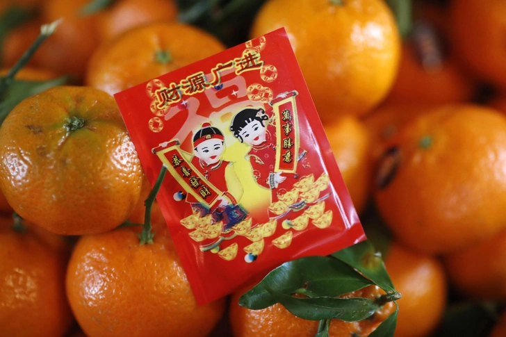 Современное фото ярких мандаринов, на которых лежит красная карточка с рисунком и китайскими иероглифами