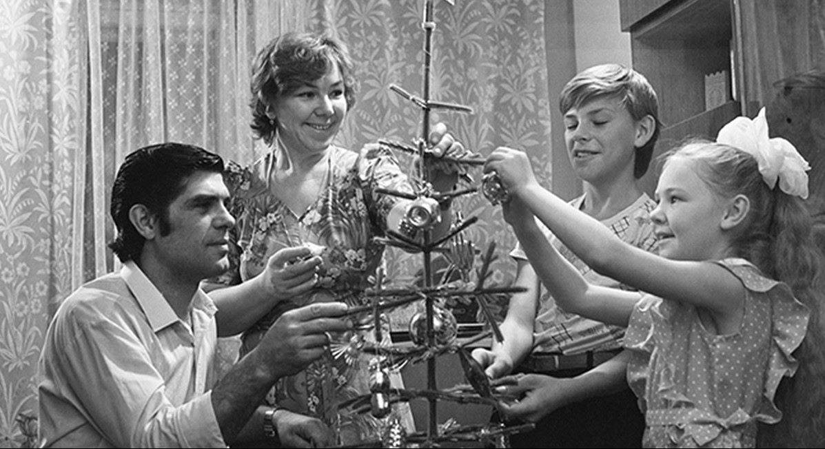 Черно-белая фотография советской семьи, украшающей новогоднюю елку в домашней обстановке