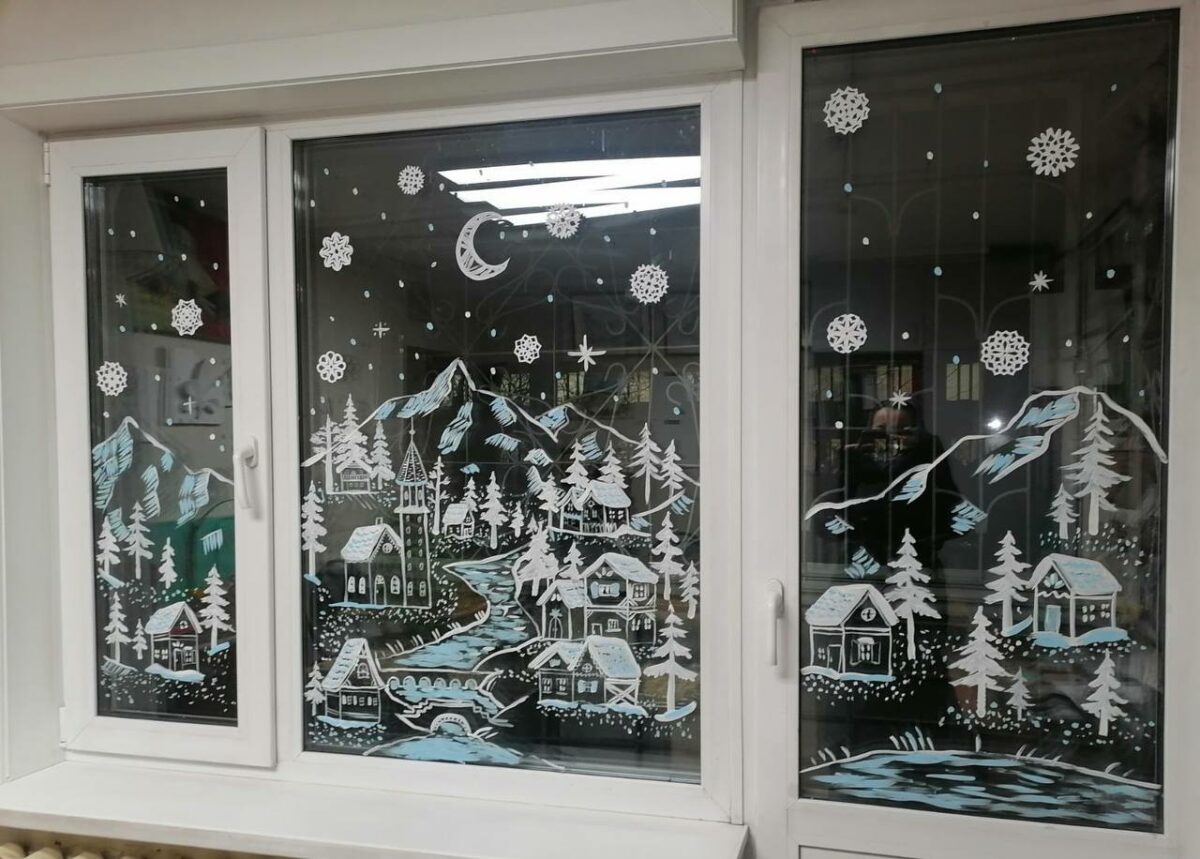 Новогодний рисунок зубной пастой на окне с зимним пейзажем и снежинками