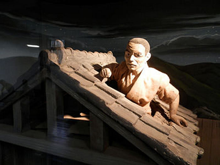 Манекен Сиратори пролезает через маленькое окно на крышу тюрьмы, вися на руках