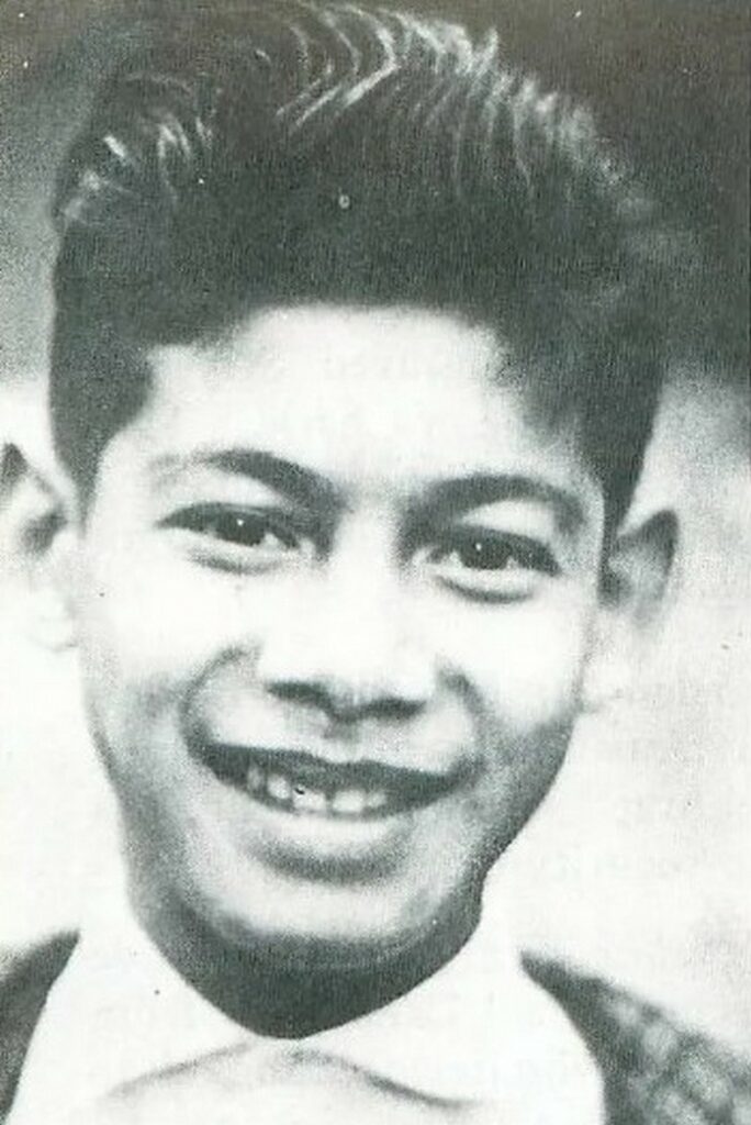 Черново-белое фото Шарля Собраджа в 11 лет с улыбкой и зачесанными волосами